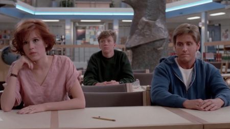 Molly Ringwald and Emilio Estevez sitting next to each other, with Anthony Michael Hall sitting behind them in The Breakfast Club