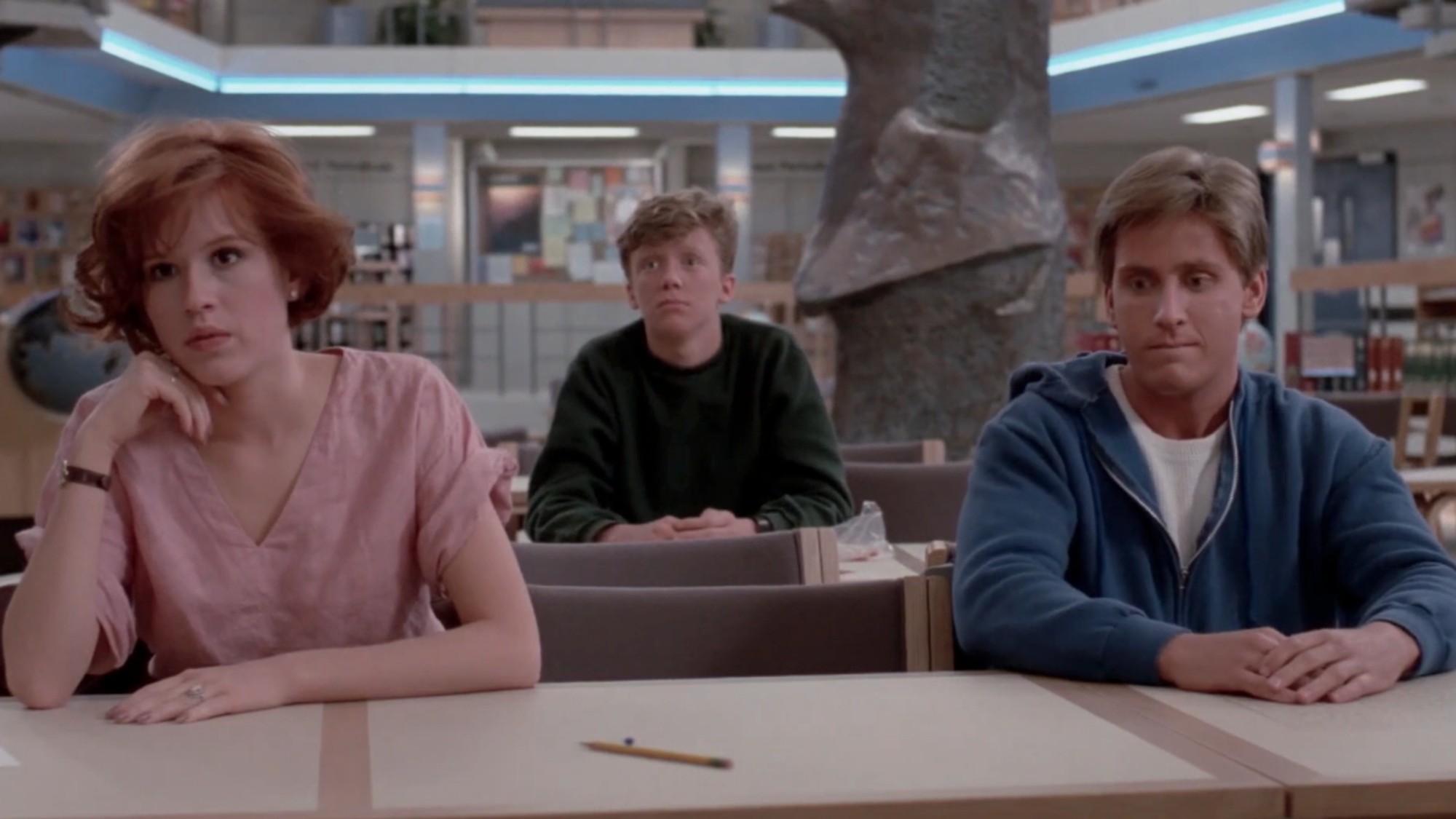 Molly Ringwald and Emilio Estevez sitting next to each other, with Anthony Michael Hall sitting behind them in The Breakfast Club
