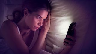 A woman looks at her phone in bed