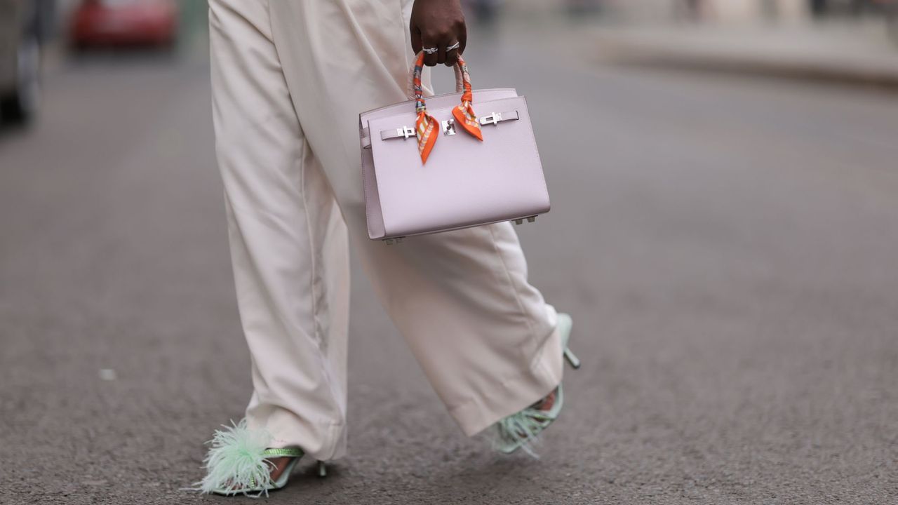 Woman wearing white trousers, green feathered shoes and a mini Hermes Birkin bag