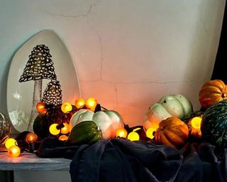 A mantelpiece with black fabric, pumpkin decorations, orange and yellow string lights, and a mushroom plate on it