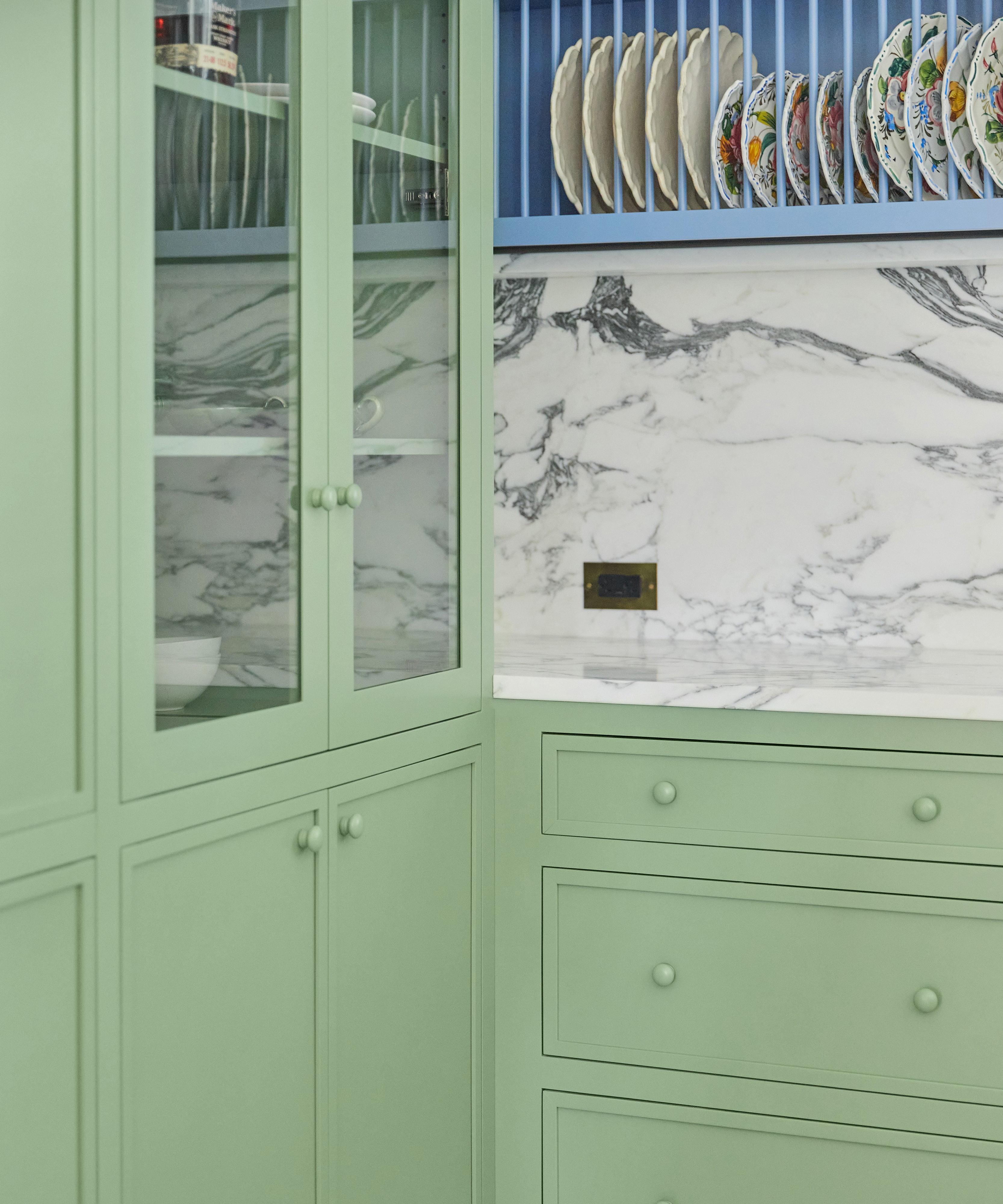 corner of a green kitchen with marble backsplash and blue plate rack