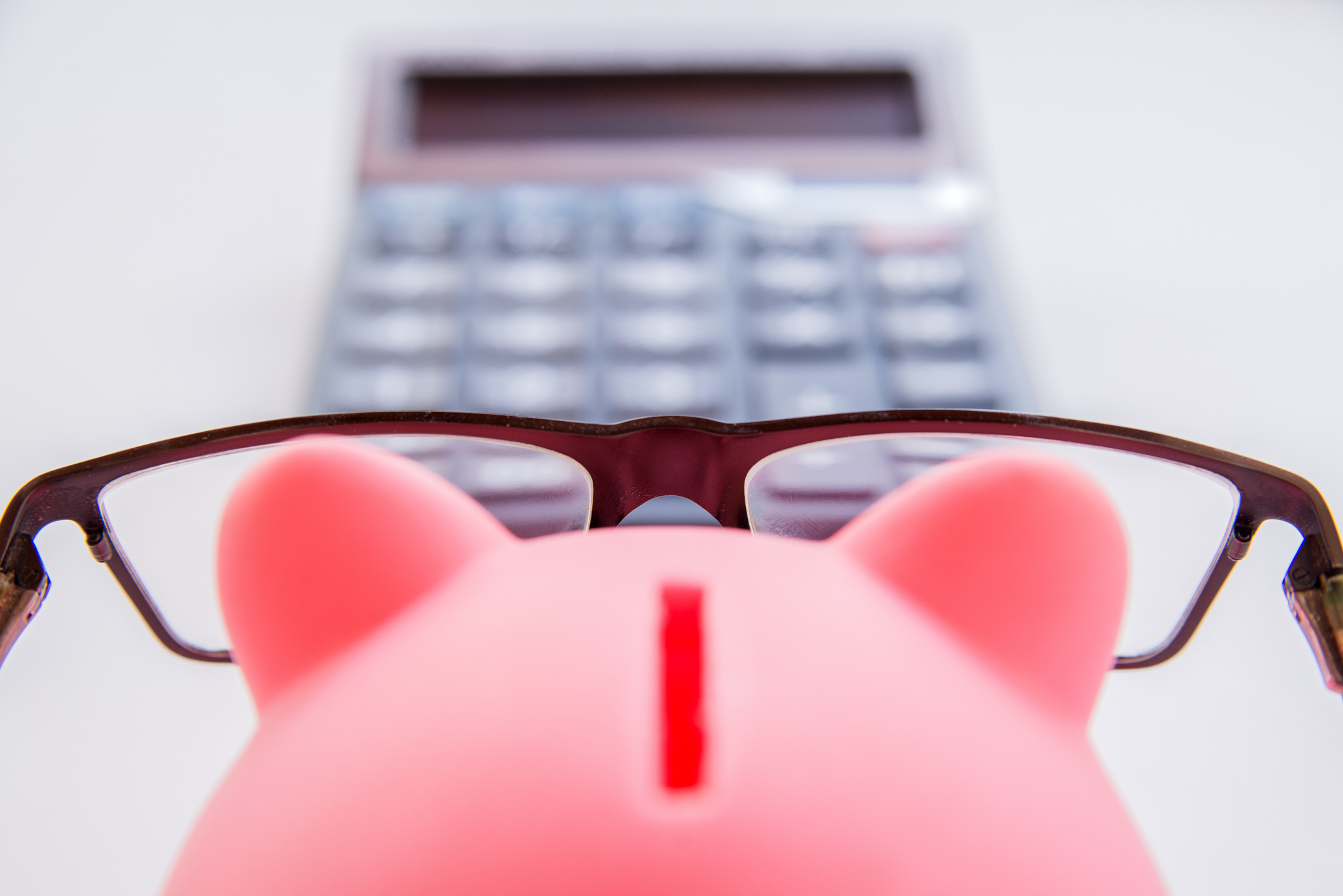 Piggy bank wearing glasses in front of a calculator.