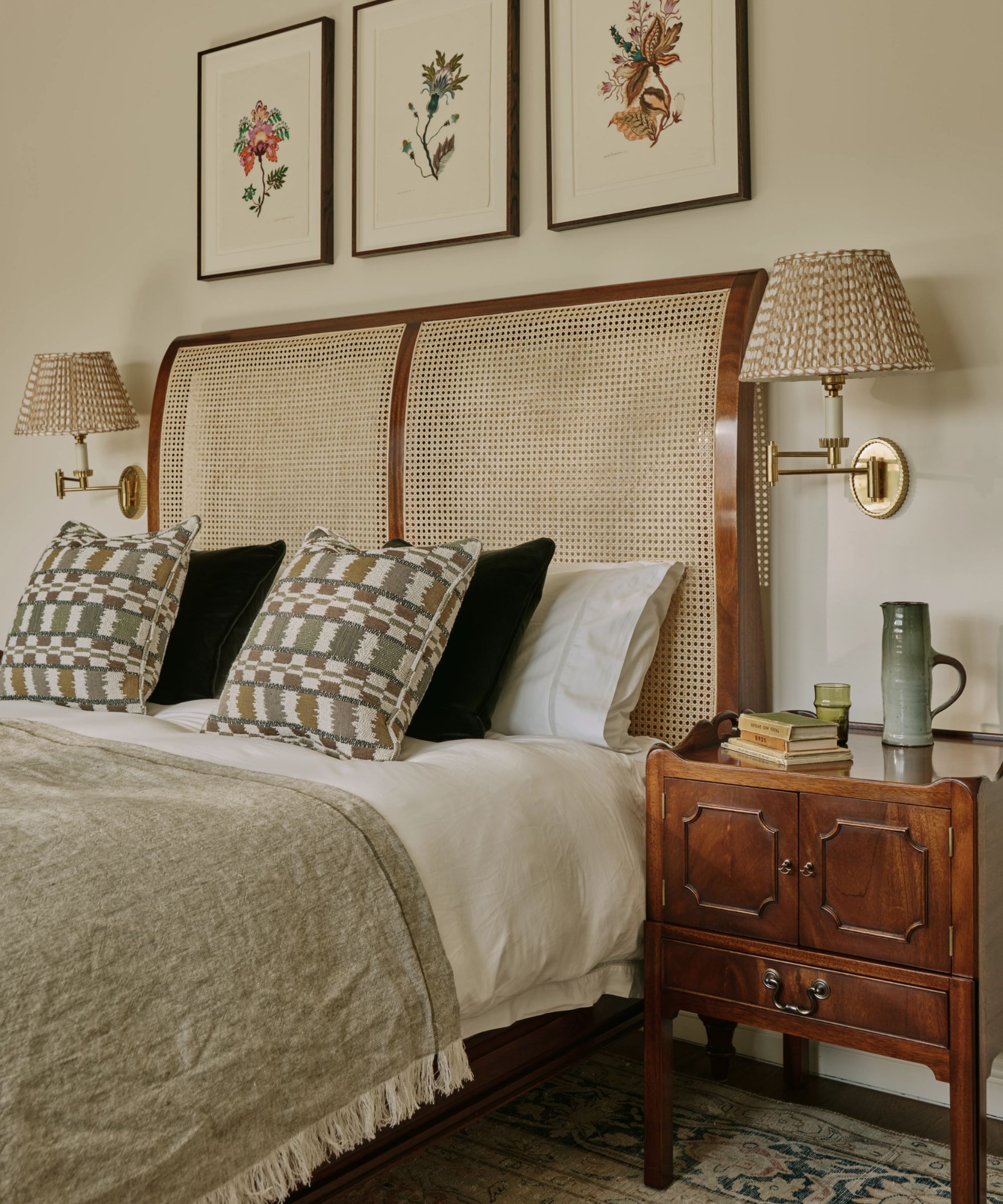 a warm neutral bedroom with a wood and rattan bed, antique chest nighstands, brass wall sconces, and linen bedding