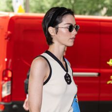 Gracie Abrams wearing a Chanel outfit that includes a cream V-neck tank with black trim, a green logo midi skirt, and a bright blue croc shoulder bag