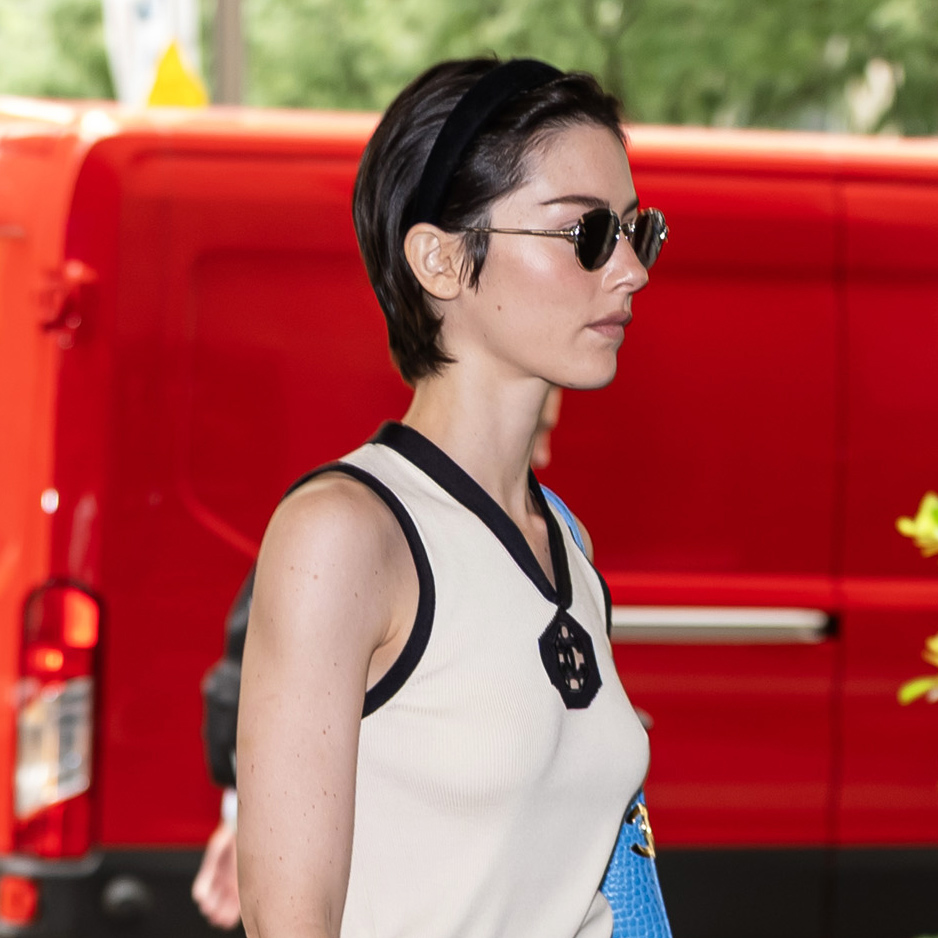 Gracie Abrams wearing a Chanel outfit that includes a cream V-neck tank with black trim, a green logo midi skirt, and a bright blue croc shoulder bag