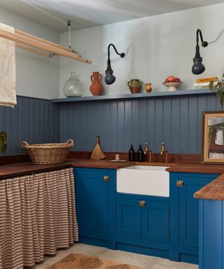 blue painted utility small kitchen with a cafe curtain wooden worktops, paneled shelving and wall lights