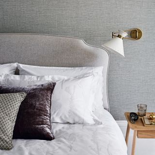 Grey bed with with white sheets, wall light and textured grey wall