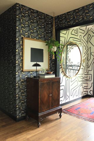 Contrasting geometric wallpapers in dark hallway and lighter lounge, complete with vintage chest and large round mirror