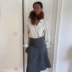 Sylvie wears a fur scarf, stripe top, and gray skirt.