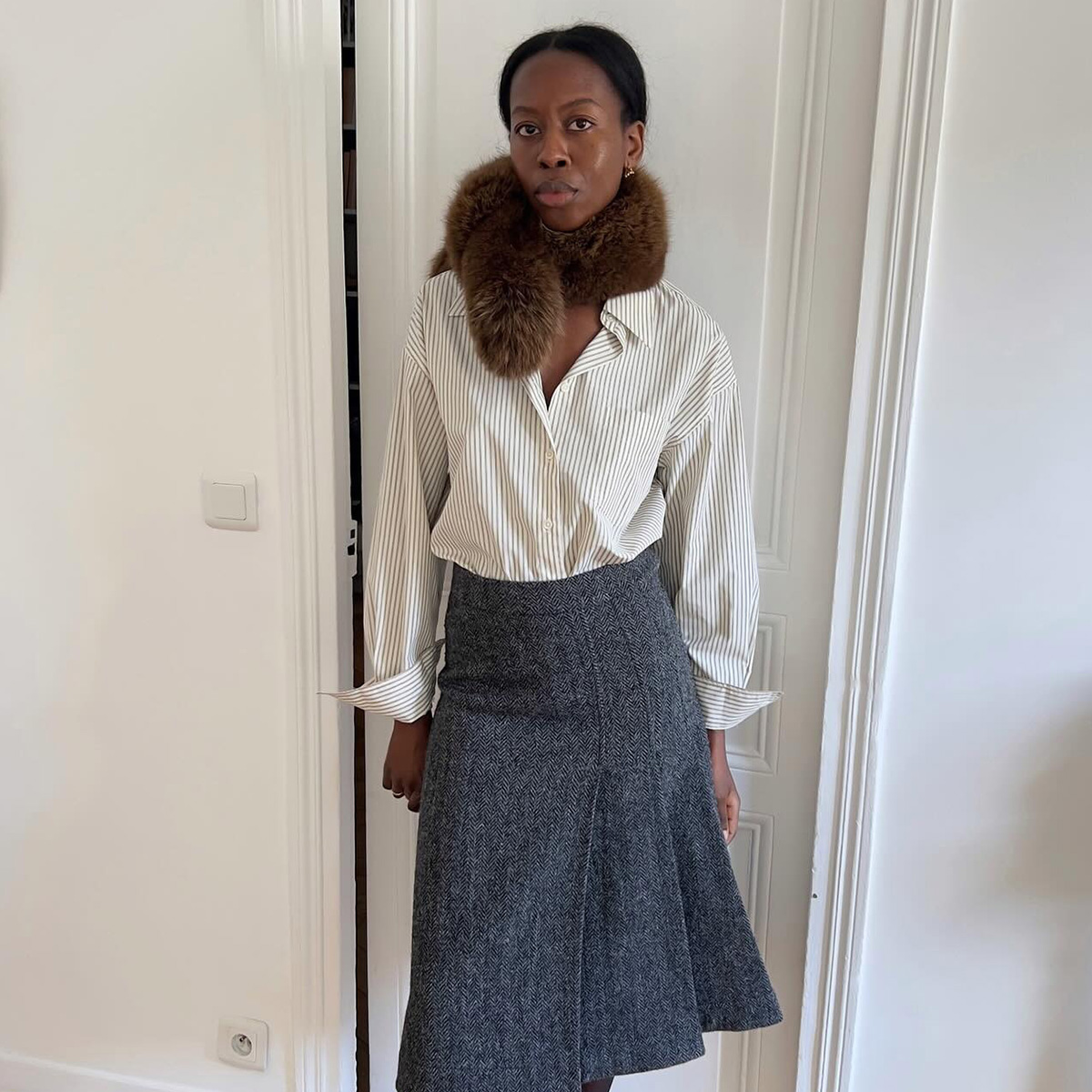 Sylvie wears a fur scarf, stripe top, and gray skirt.