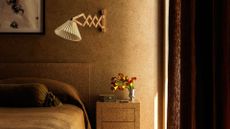 A bedroom with ochre interiors, thick drapery and wall lamp