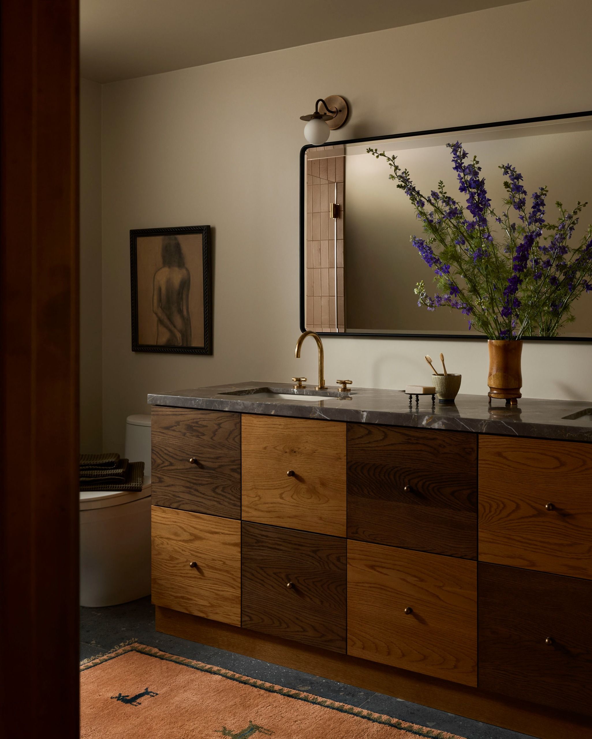 A modern bathroom with a large-format checkerboard double vanity with a stone countertop and a large mirror above it with artwork to the left