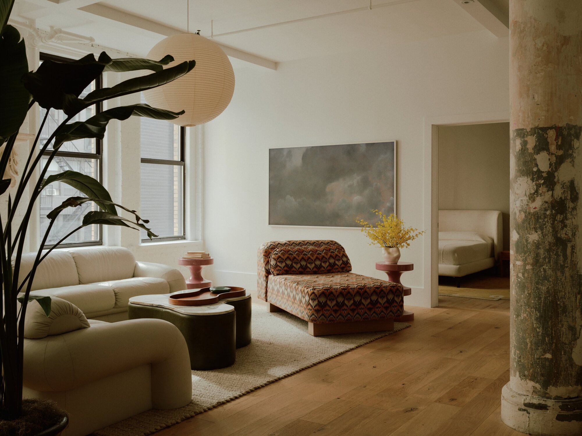 modern loft-style living room with timber floors, beige rug, beige corner sofa, patterned chaise lounge, round coffee table, artwork on wall, and paper lantern hanging overhead