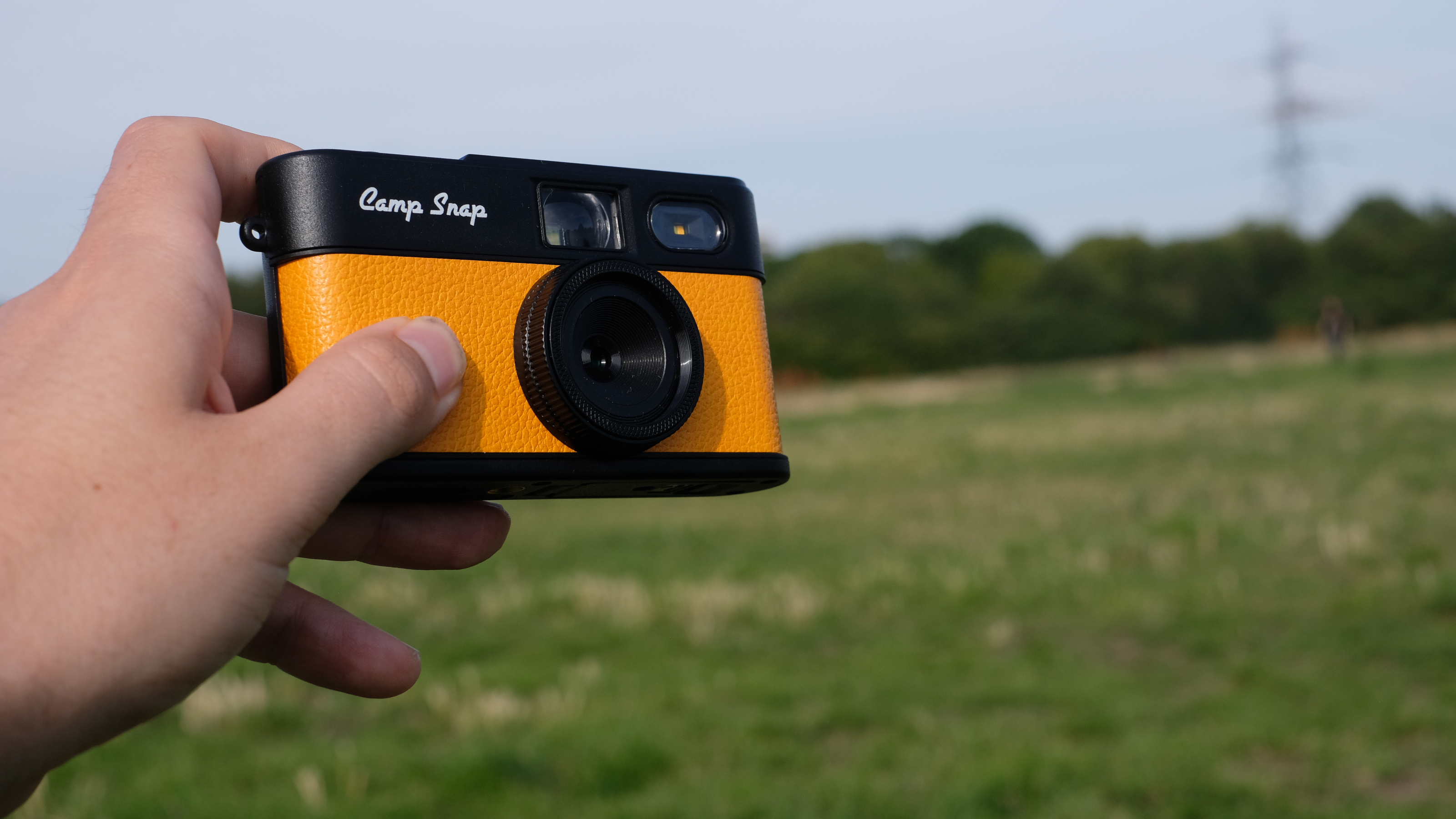 Photograph of man's hand holding Camp Snap 2 digital camera, in yellow colorway