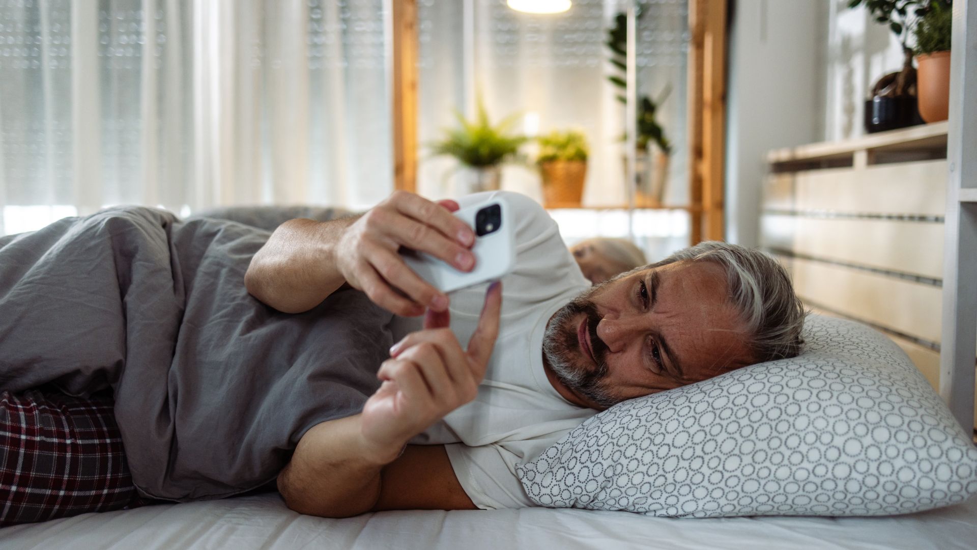 man using smartphone in bed away from wife