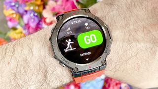 The Amazfit T-Rex 3 shown close-up on a user's wrist with the snorkeling and surfing workout tracking modes displayed; colorful flowers are out of focus in the background