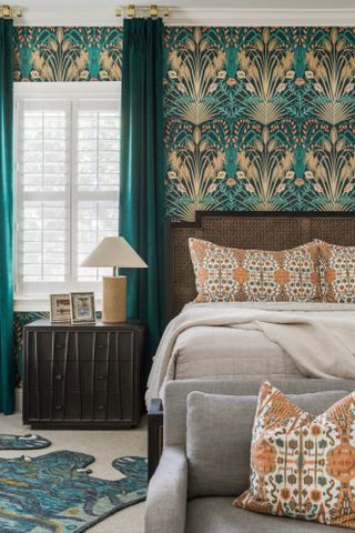 Bedroom with teal and gold patterned wallpaper, wooden bed, orange patterned cushions , teal curtains and white shutters