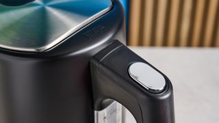 an all-black ninja electric kettle with a precision temperature base for specialty tea and general kitchen use, close up of the handle with a silver button