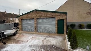 A garage with metal doors and wooden cladding walls with artificial plants around it