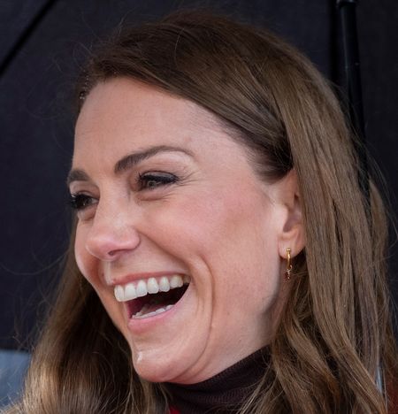 Kate Middleton smiling standing under an umbrella