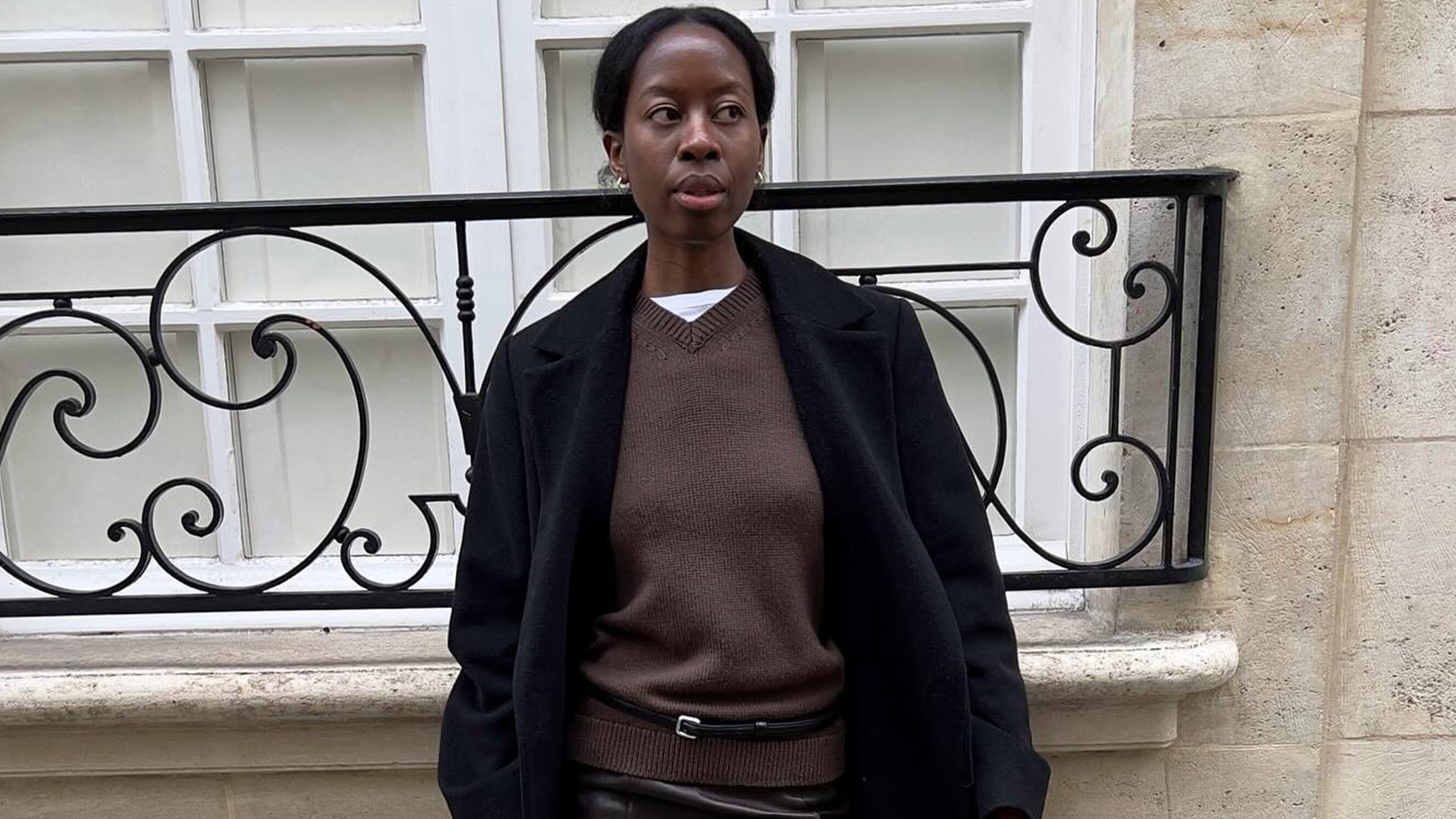 Influencer Sylvie Mus wearing brown cashmere sweater, white t-shirt, black coat, and grey skirt in Paris.