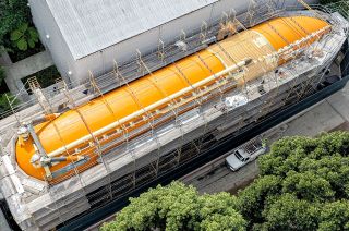 a space shuttle's orange external fuel tank is surrounded by scaffolding and fencing
