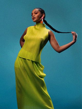 Celeste O'Connor wears green mock neck top and matching skirt holding braided hair in hand.