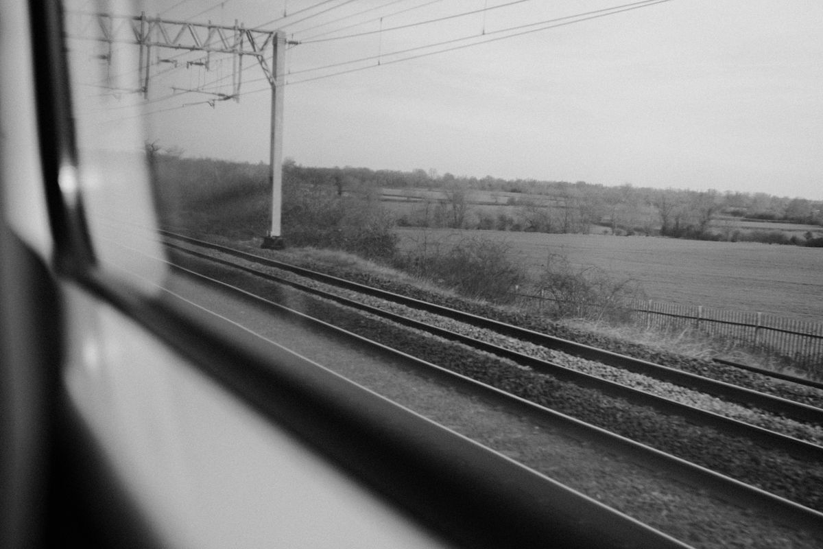 Black-and-white view from a train window across railway tracks and fields