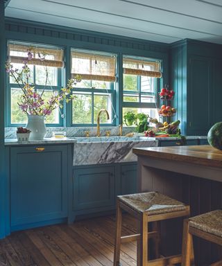 blue kitchen with dark wooden floors and a sink made of marble with three windows with chik blinds