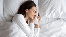 A woman with long dark hair sleeps happily on her side on a white cooling mattress