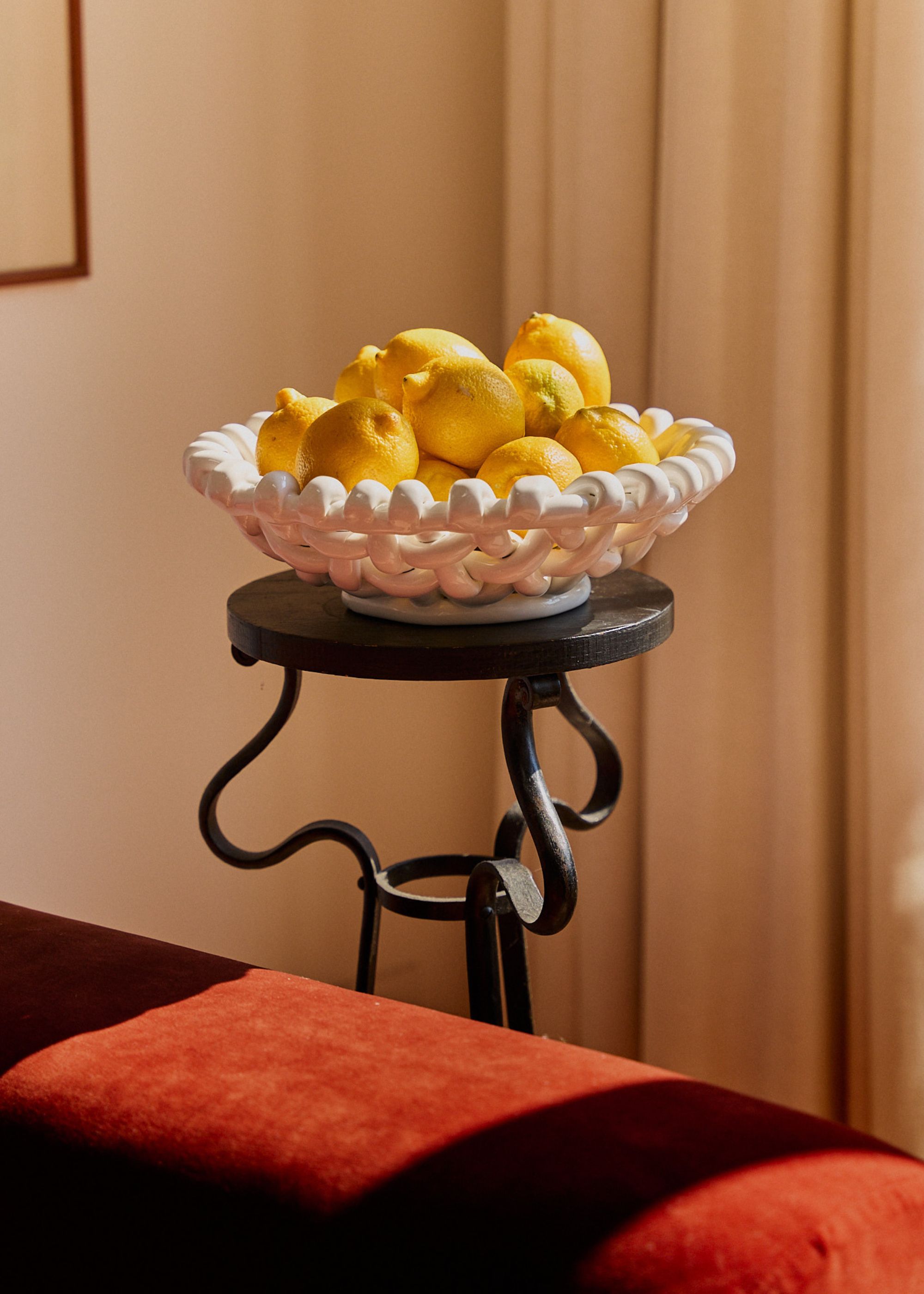 A white basketweave bowl on a stand with lots of lemons inside of it