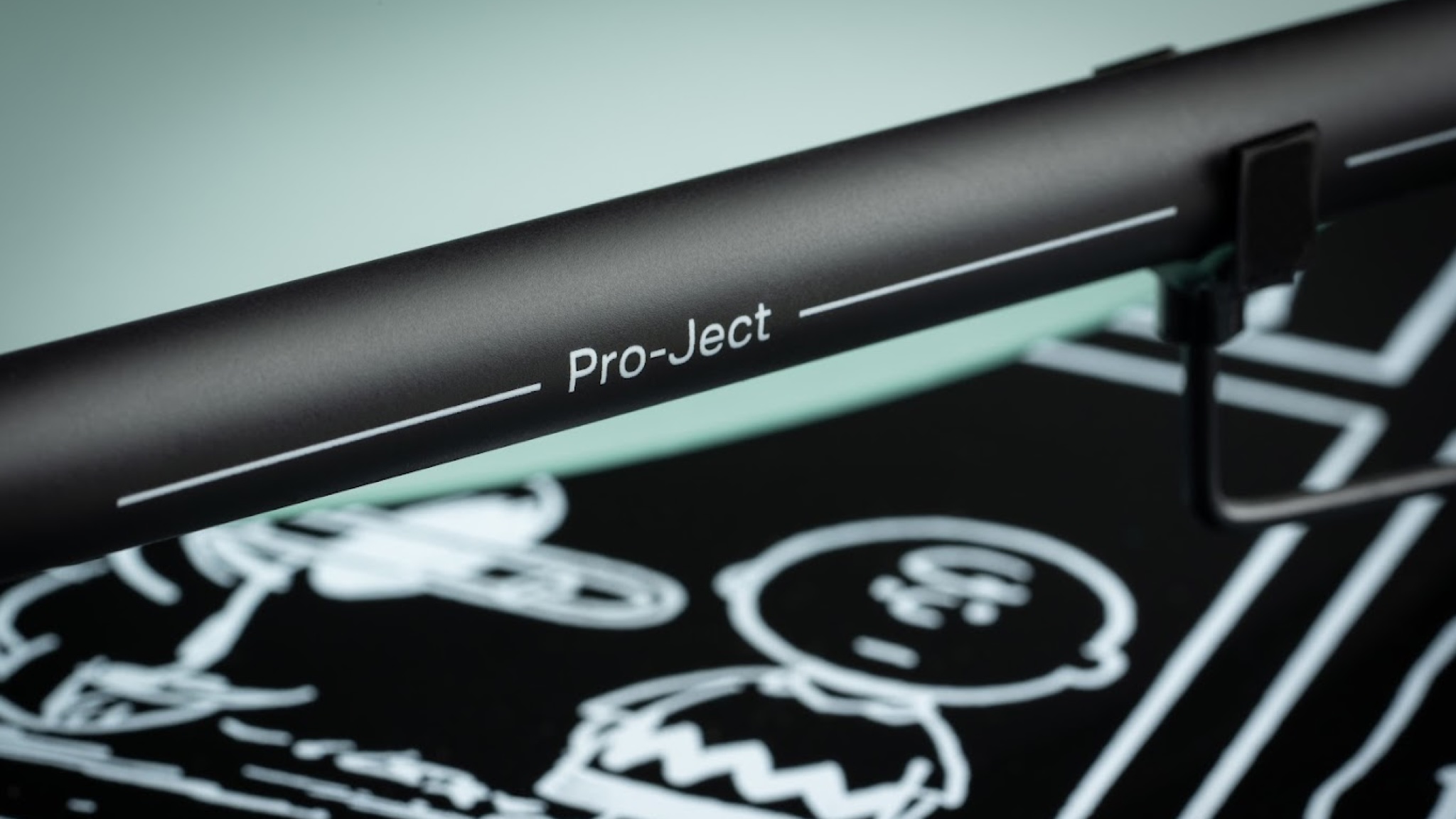 Pro-Ject Peanuts turntable with a close-up of the tone arm. Part of a Peanuts panel is visible below but slightly blurred.
