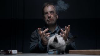 Bob Odenkirk smoking cigarette with cat in front of him in Nobody