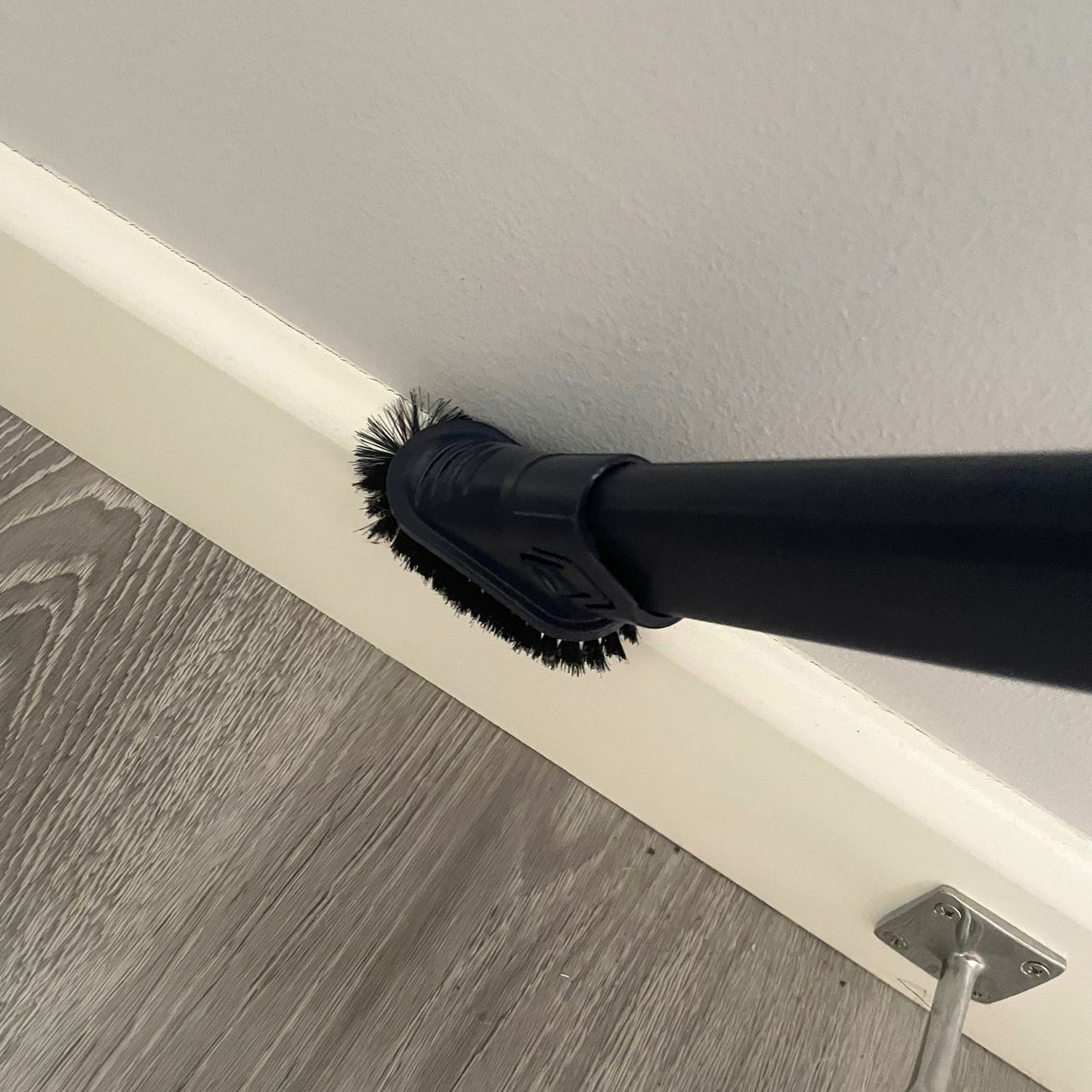 Using a vacuum duster tool to dust white skirting boards