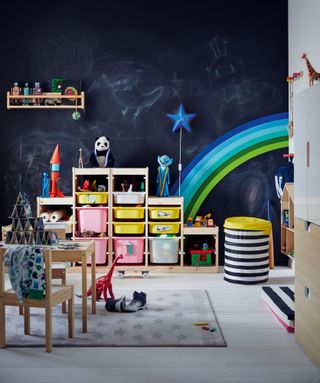 kid's playroom with chalkboard wall and rainbow mural, and a wood and color storage unit, a rug on the white floor, and a wooden small dining set, with table and chairs