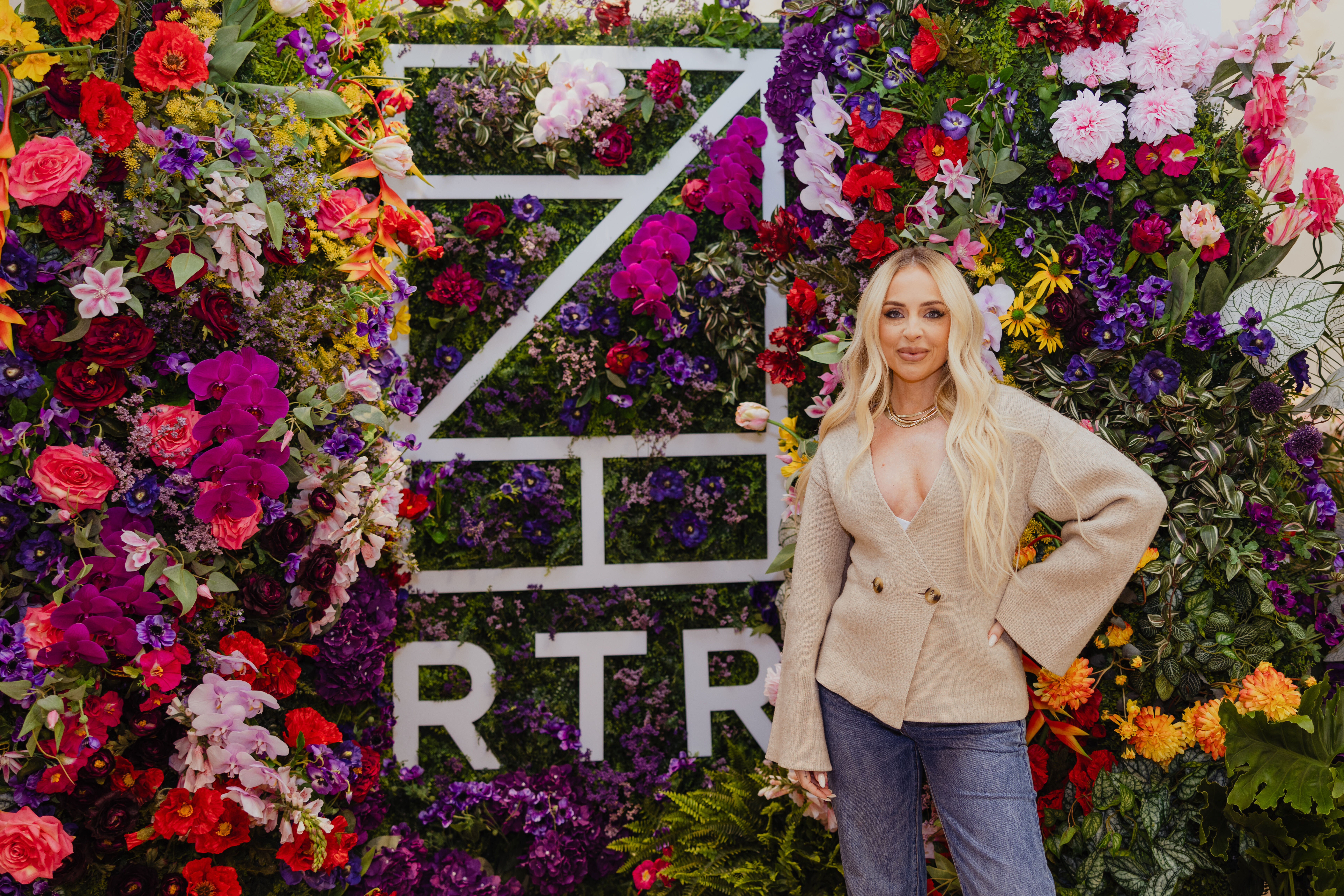 Stylist Maeve Reilly stands in tan blazer and jeans next to colorful Rent the Runway signage.