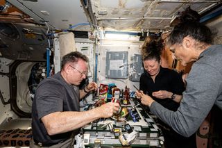 three astronauts on board the international space station gather around a small dinner table