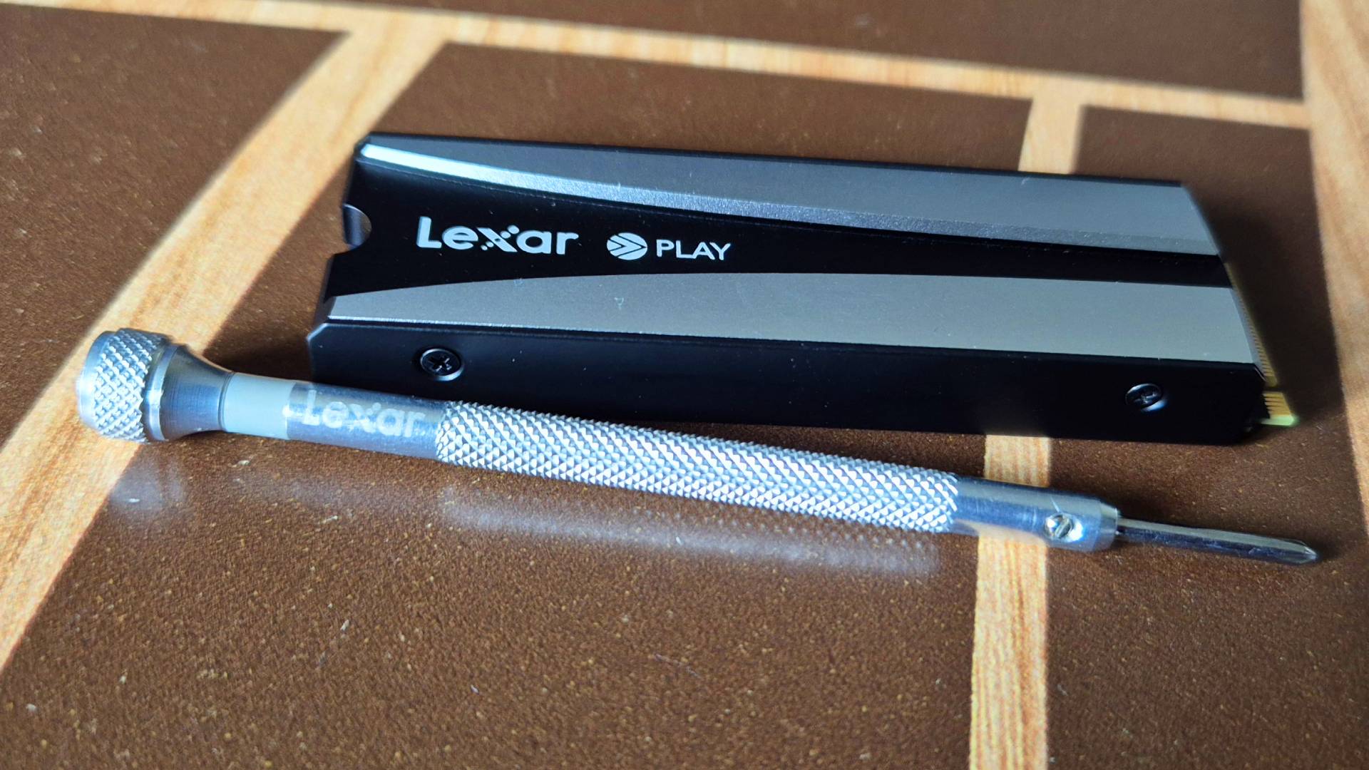 Photo by Rosalie Newcombe of the Lexar Play 2280 SE PCIe 4.0 PS5 SSD, sitting on a wooden coffee table.