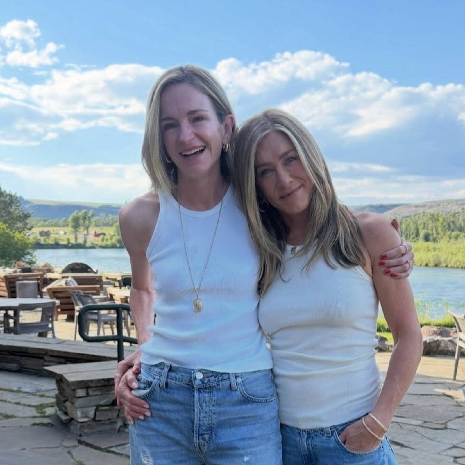Jennifer Aniston poses with Molly Kimmel lakeside, both wearing white tank tops and jeans.