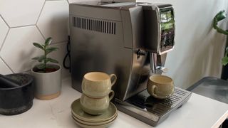 The side of the De’Longhi Dinamica Plus coffee maker on a kitchen countertop with a cup ready to pour an espresso