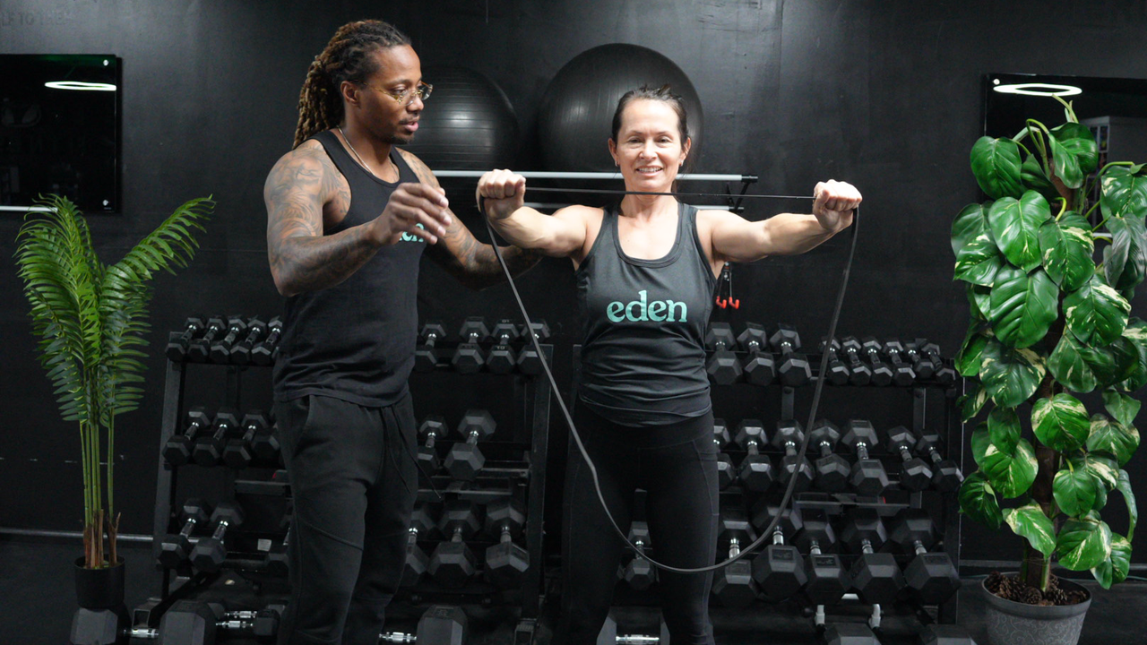 NASM-certified personal trainer Brandon Polk coaches a female client, who demonstrates band pull-aparts
