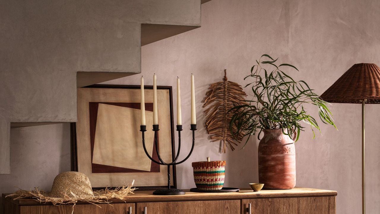 A sideboard with a candlestick and vase of greenery set against a limewashed wall