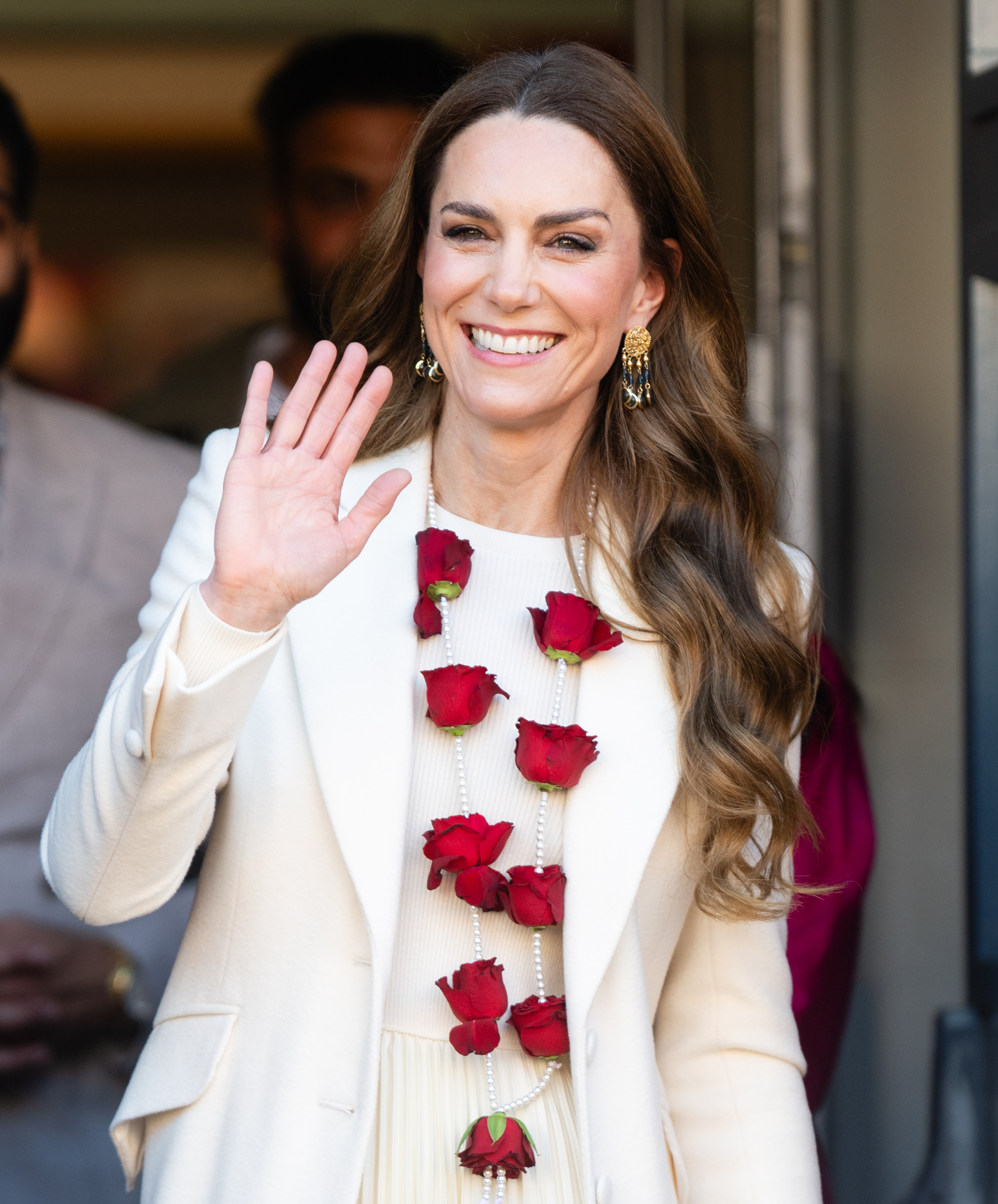 Princess Kate wearing a red rose garland and a white coat waving