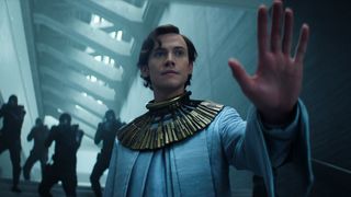 Brother Dawn holding up his left hand as Empire soldiers stand behind him with guns raised in Foundation season 3 episode 5