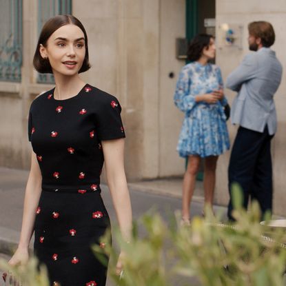 lily collins as emily wearing a black and red polka dot dress turning around her shoulder surprised on a european street in season 5 of emily in paris
