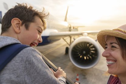 A happy boy and his mother stand on the tarmac about to board an airplane.