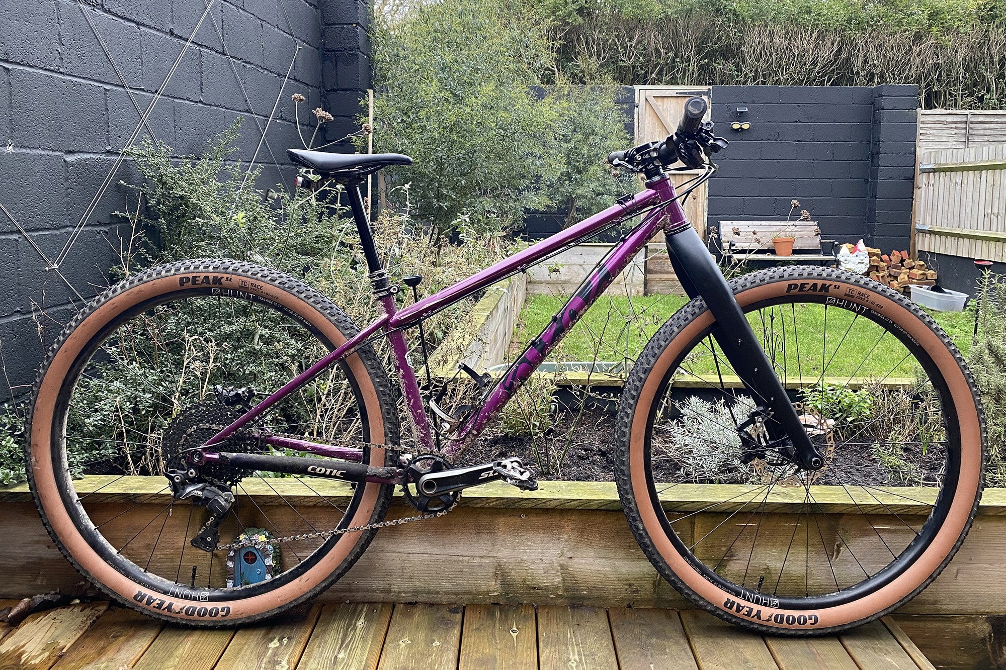 Un Cotic Solaris Max 2018 violet équipé d'une fourche rigide en carbone, de pneus à flancs Goodyear marron avec un petit fond de jardin