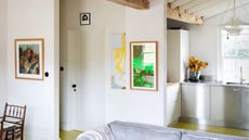 An open plan kitchen and living area with white walls, stainless steel cabinetry and art work on all of the walls