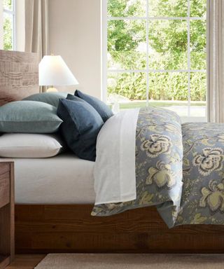 Side view of white and blue bedding on a dark wood bed frame; in the background, white walls and windows looking onto the garden.